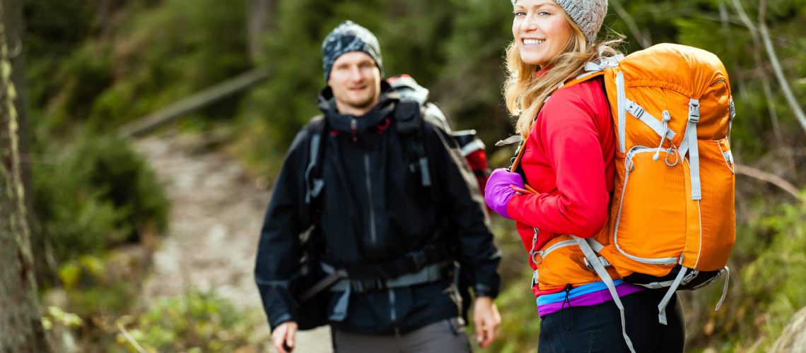 Man and woman hikers trekking in mountains. Young couple walking with backpacks in forest, Tatra Mountains in Poland. Trekking hiking outdoors in beautiful nature